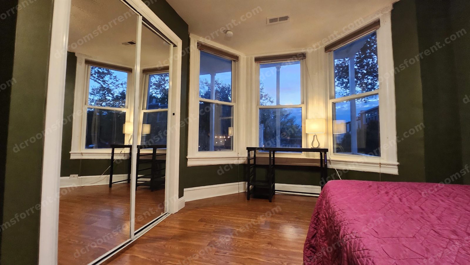 Delta Room at dusk: desk and lamp under the bay window, bed in the corner