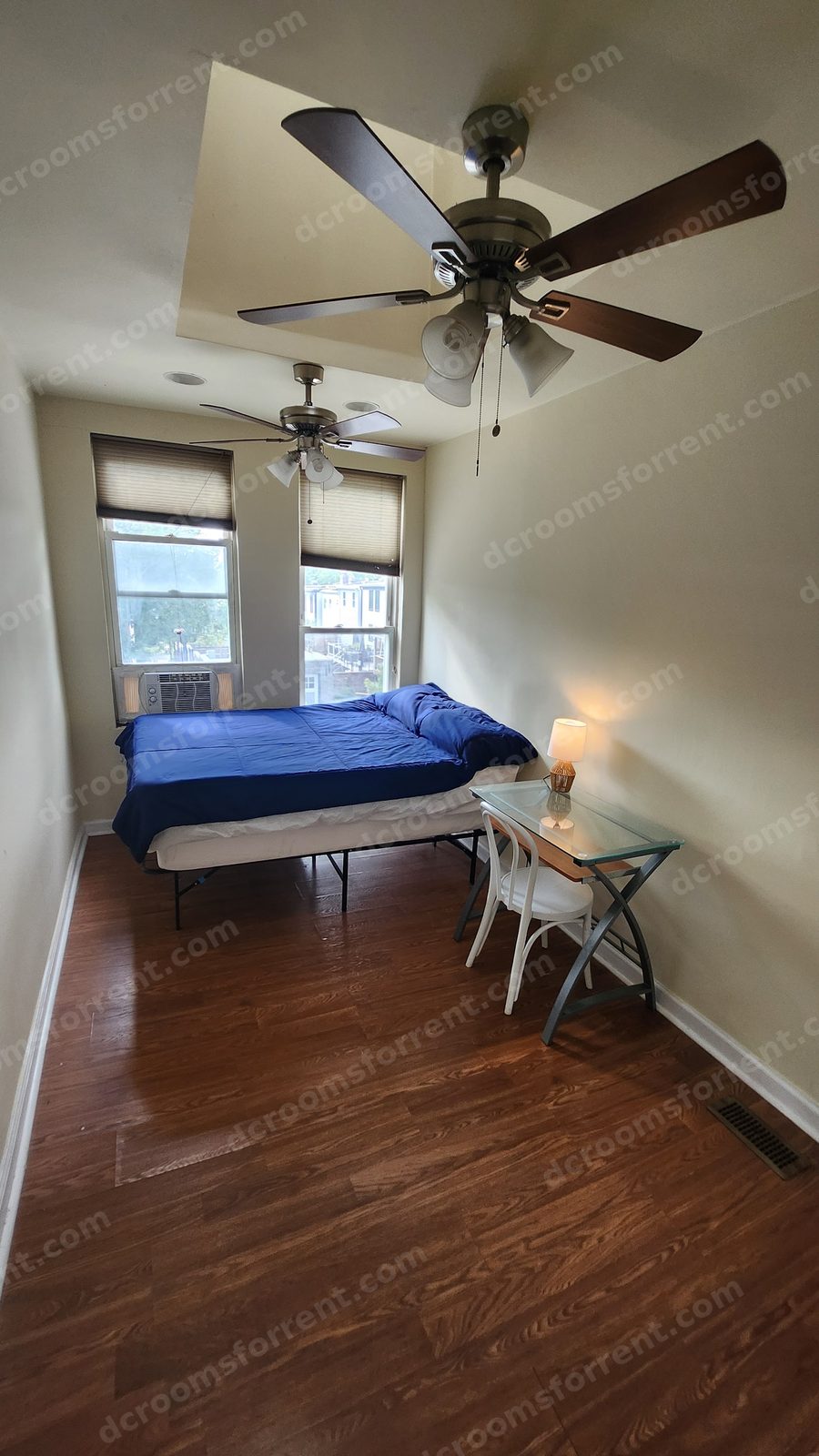 Foxtrot Room: bed with blue bedspread under the skylight, two tall windows with natural light, glass desk with lamp