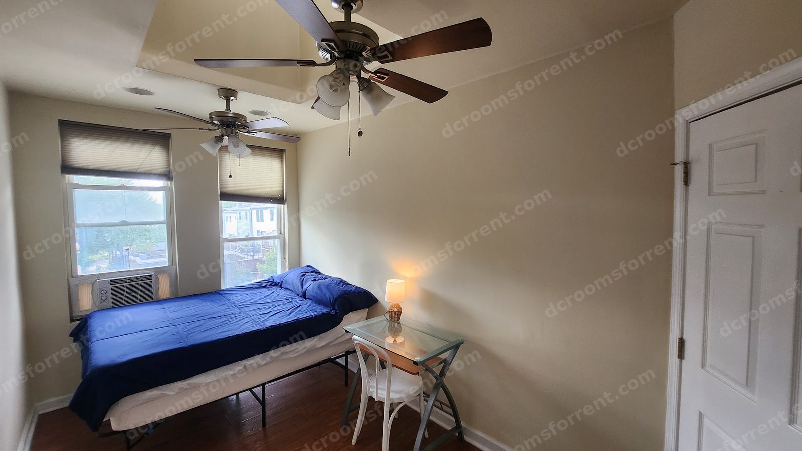 Foxtrot Room: bed with blue bedspread, two tall windows, glass desk with lamp, skylight and ceiling fans above