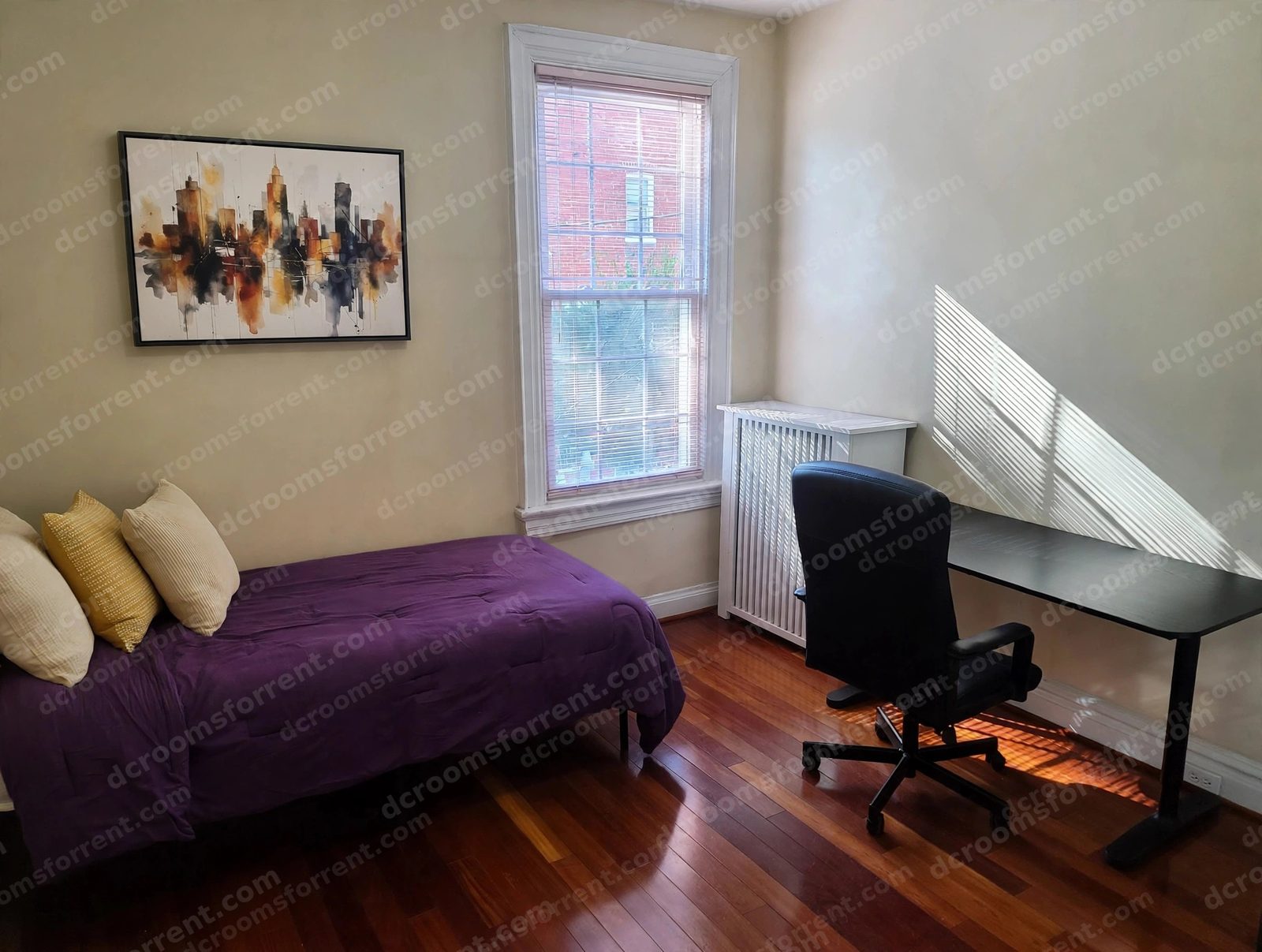 Staged Joey Room with purple bedspread, pillows, wall art, window, desk and office chair.