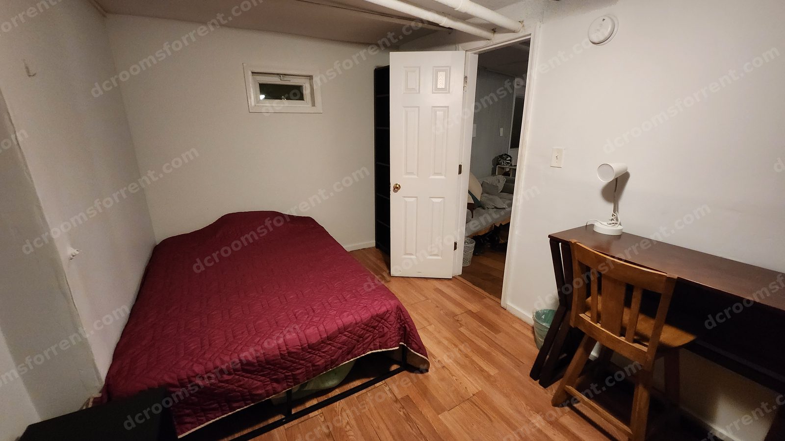 Furnished Lincoln Room with burgundy bedspread, wood desk with lamp and chairs, closet alcove, and door open to the hallway.