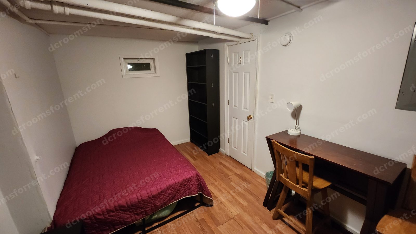 Lincoln Room with burgundy bedspread, wood desk and chair, tall black bookshelf, and ceiling fan with light.