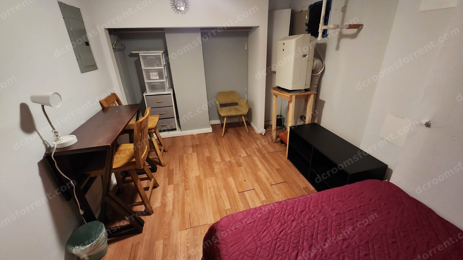 Lincoln Room desk corner with lamp and chairs, closet storage drawers, armchair, and portable air conditioner.