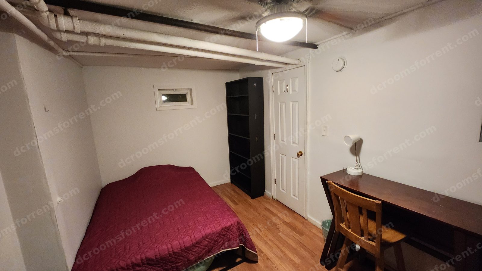 Lincoln Room with bed, desk and chair, bookshelf, and closed door under the ceiling fan light.