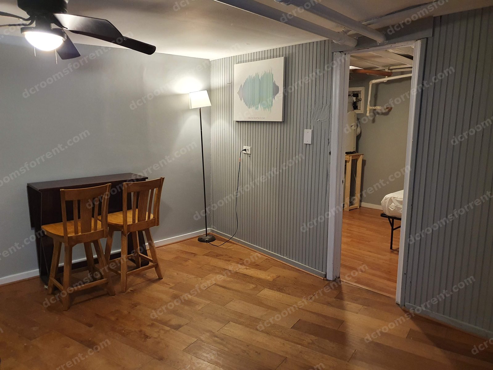 Shared living/dining area with drop-leaf table and stools, floor lamp, and wall art; Lincoln Room visible through the open doorway.
