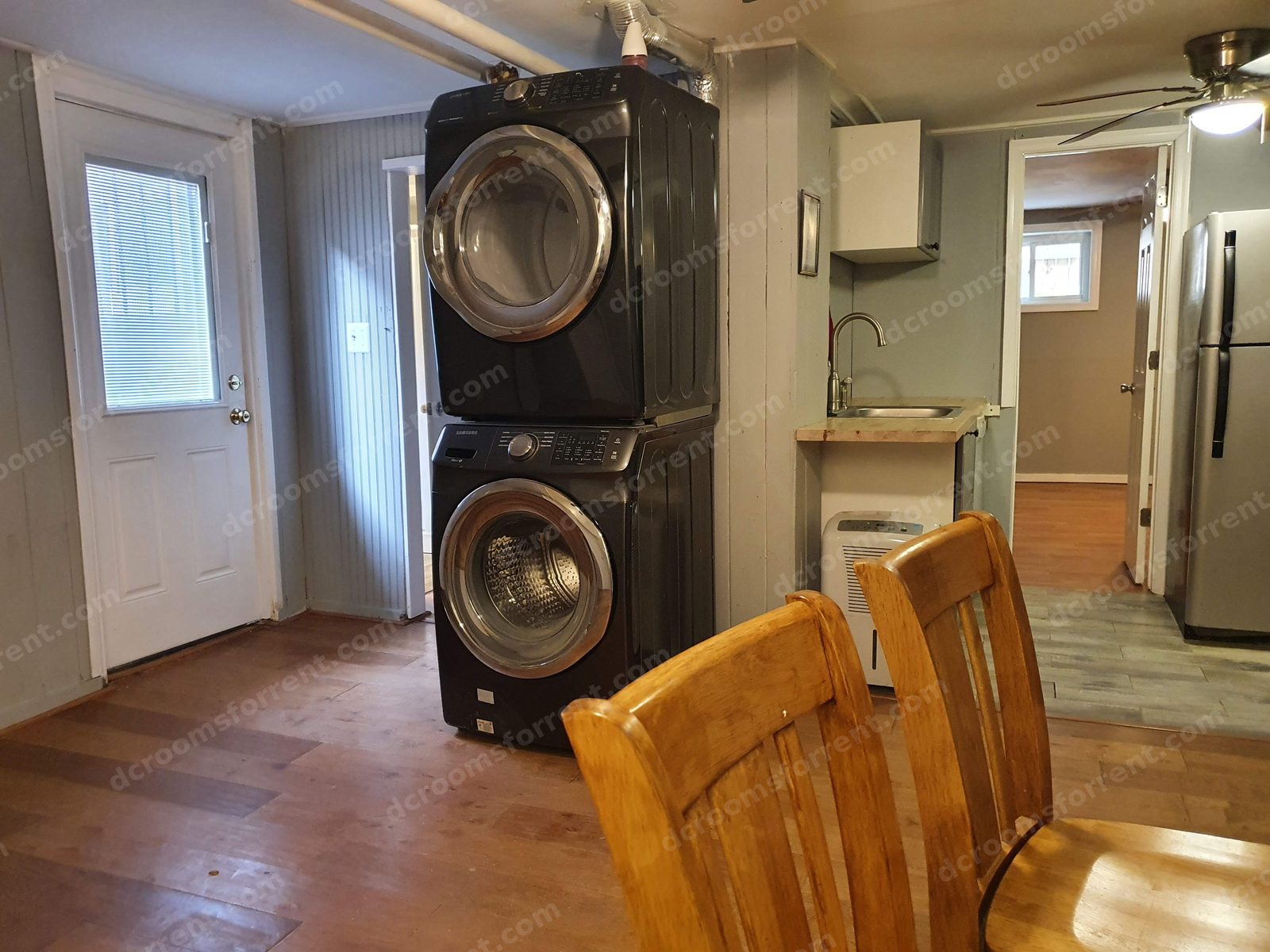 Stacked washer and dryer in the common area with back door and kitchenette sink nearby.