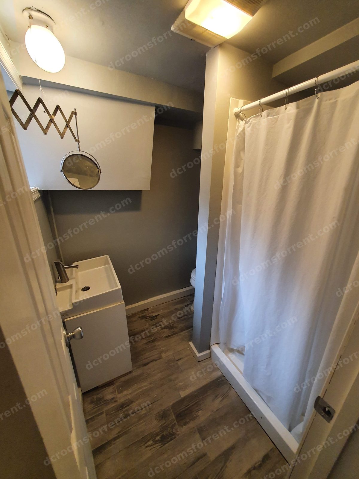 Shared bathroom with vessel sink, wall mirror, toilet, and shower with white curtain.
