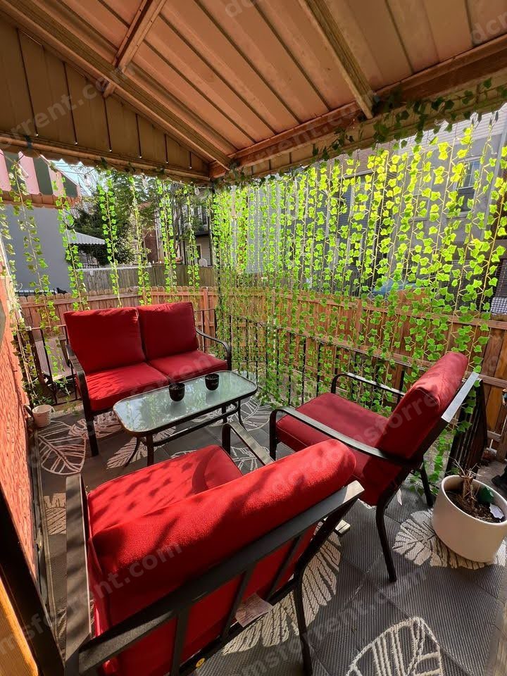 Covered patio with red chairs, table, and hanging ivy.
